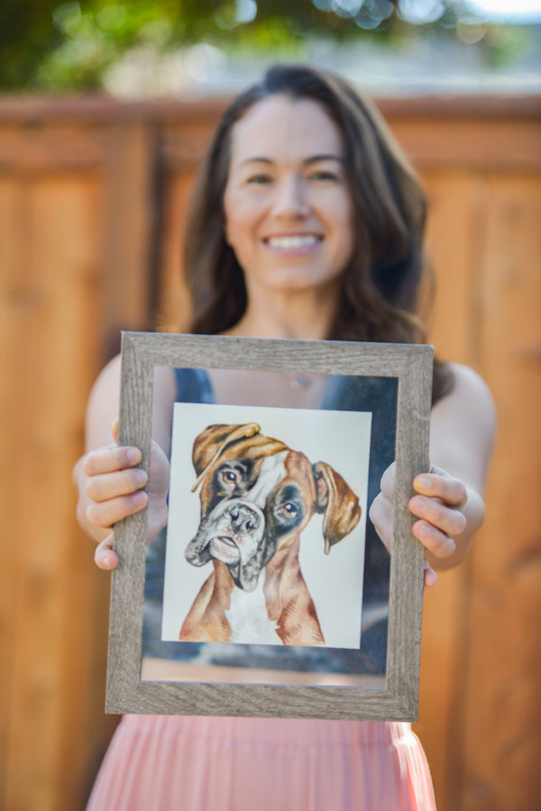 Lauren Salas, the artist, holding two framed watercolor portraits