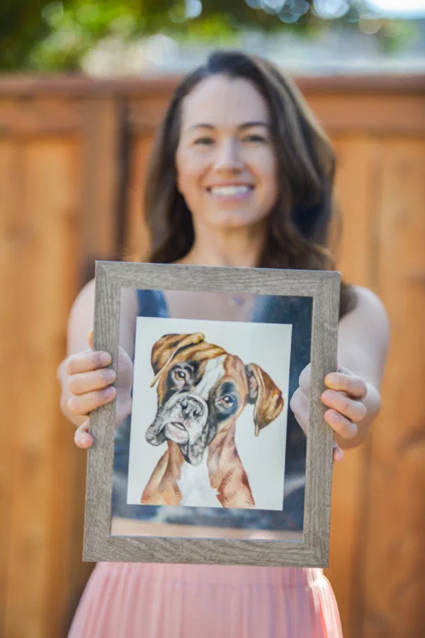 Lauren Salas, the artist, holding a framed watercolor dog portrait