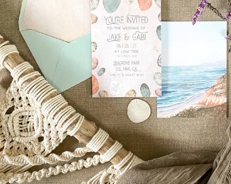 Coastal watercolor wedding invitation with a beach scene and sage-green envelope